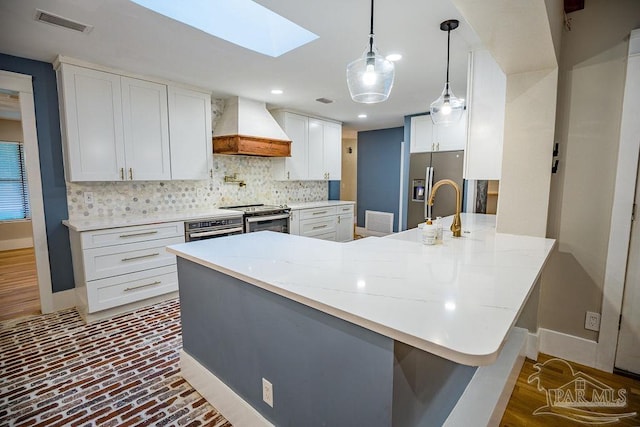 kitchen featuring white cabinetry, appliances with stainless steel finishes, kitchen peninsula, custom range hood, and a skylight