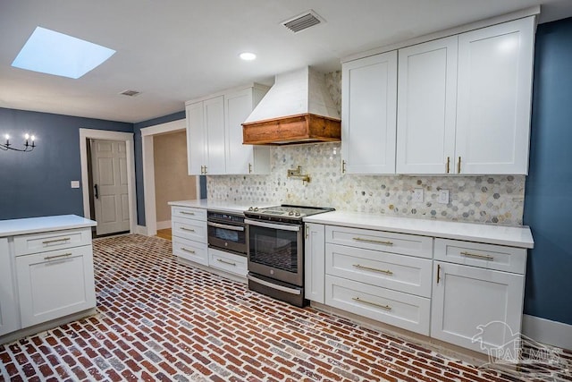 kitchen with white cabinets, tasteful backsplash, custom exhaust hood, a skylight, and appliances with stainless steel finishes