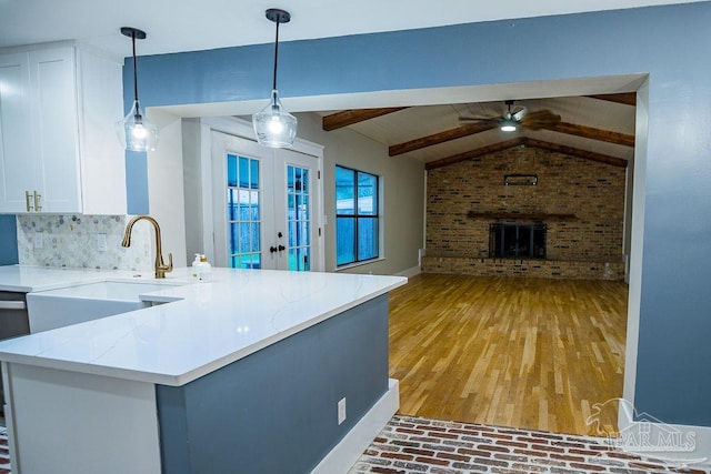 kitchen featuring french doors, kitchen peninsula, light stone countertops, a fireplace, and decorative light fixtures