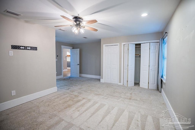 unfurnished bedroom featuring ceiling fan, light carpet, and two closets