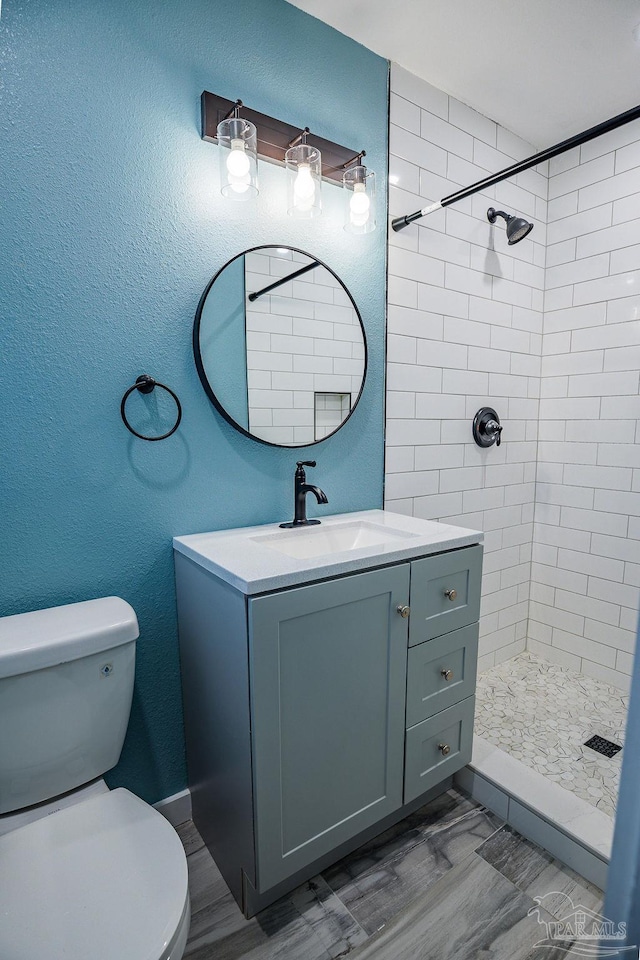 bathroom featuring toilet, vanity, and a tile shower