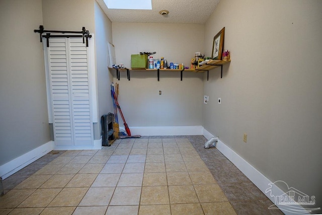 clothes washing area with hookup for an electric dryer, light tile patterned floors, a textured ceiling, and a skylight