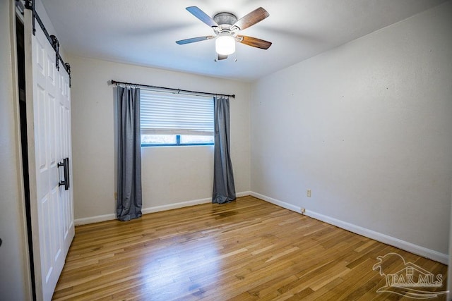 unfurnished room with light wood-type flooring, a barn door, and ceiling fan