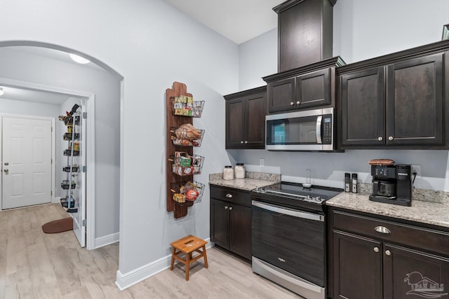6743 Desoto St, Navarre, FL 32566 - kitchen featuring appliances with stainless steel finishes, light wood-type flooring, arched walkways, light stone countertops, and dark brown cabinetry