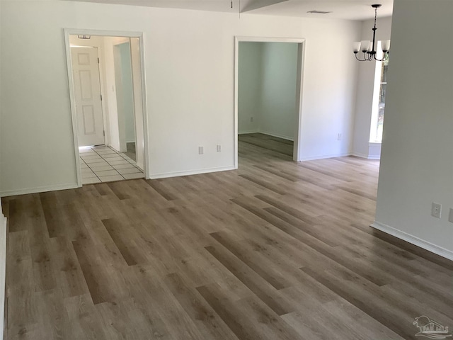 spare room with a chandelier, wood finished floors, and baseboards