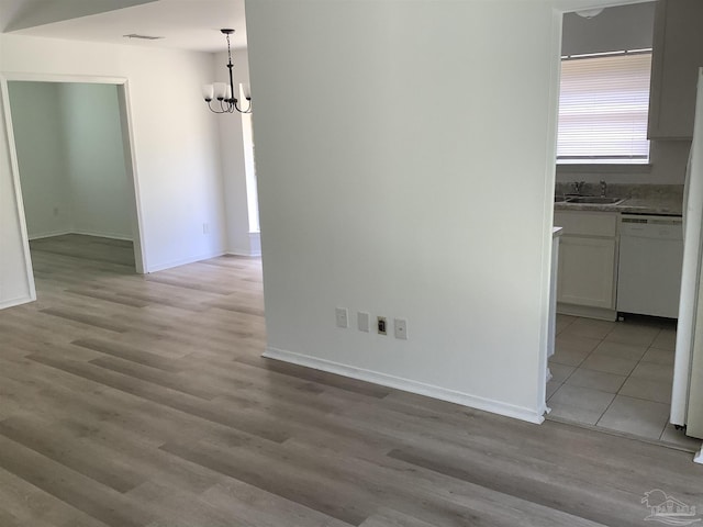 unfurnished dining area with a sink, a chandelier, and light wood-style flooring