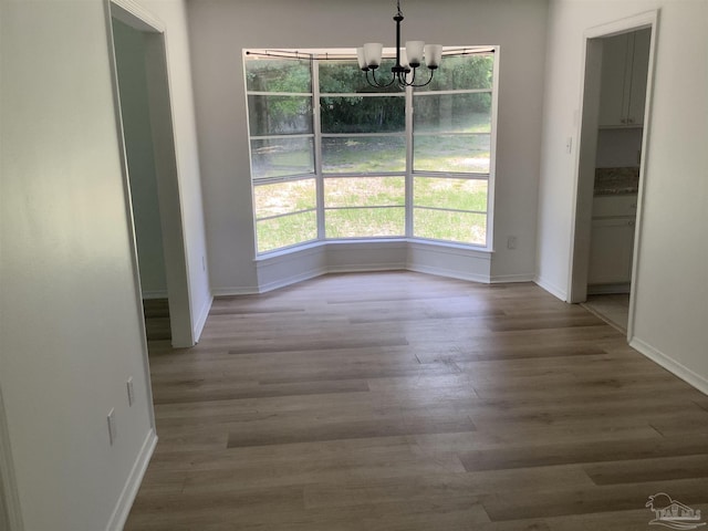 unfurnished dining area with baseboards, a chandelier, and wood finished floors