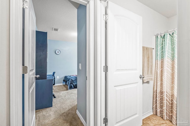 hall with a textured ceiling and light colored carpet