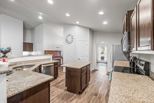 kitchen featuring light stone counters, stainless steel appliances, sink, light hardwood / wood-style floors, and an island with sink