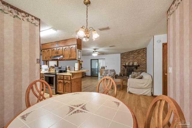 dining room with visible vents, a fireplace, wallpapered walls, light wood finished floors, and ceiling fan with notable chandelier