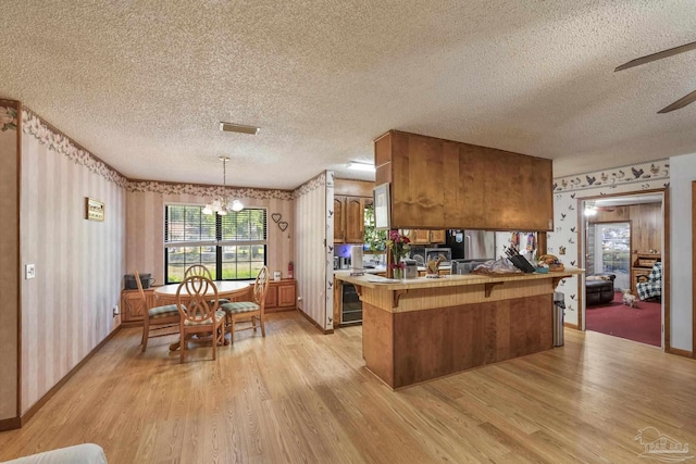 kitchen with brown cabinets, light wood-style floors, a kitchen breakfast bar, a textured ceiling, and wallpapered walls
