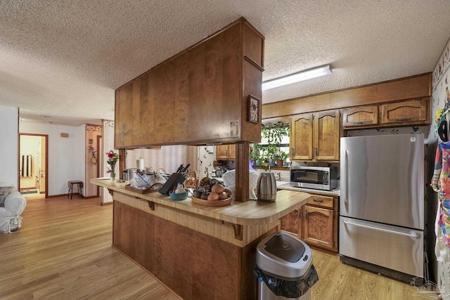 kitchen with a textured ceiling, light wood finished floors, brown cabinets, and stainless steel appliances
