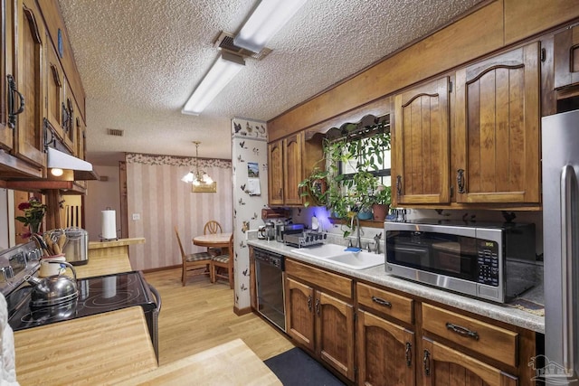 kitchen featuring a textured ceiling, a sink, light countertops, black appliances, and light wood-style floors