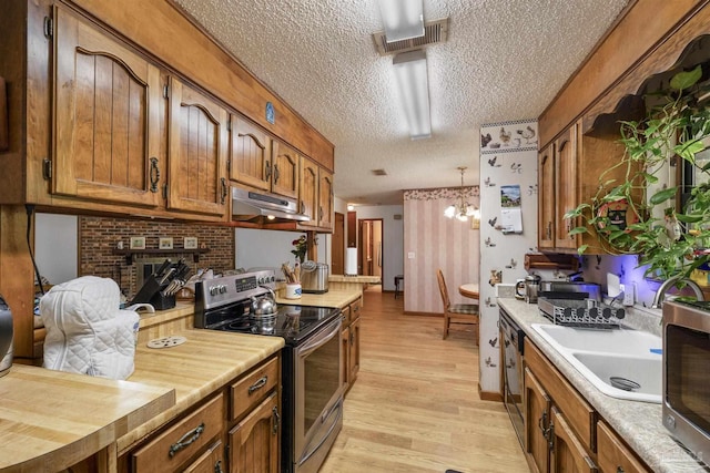 kitchen featuring light wood finished floors, a textured ceiling, brown cabinetry, stainless steel appliances, and under cabinet range hood