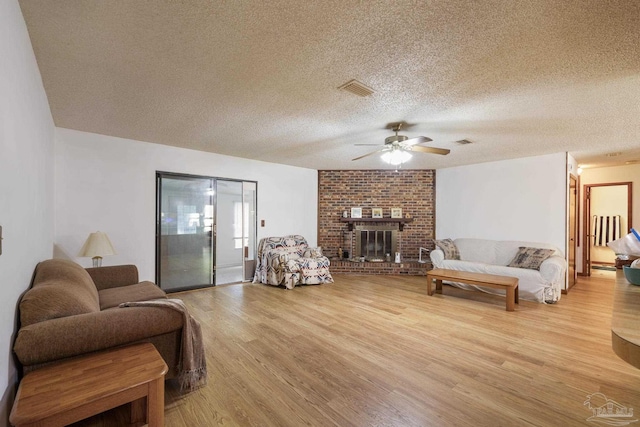 living room with a textured ceiling, ceiling fan, light wood-style flooring, and visible vents