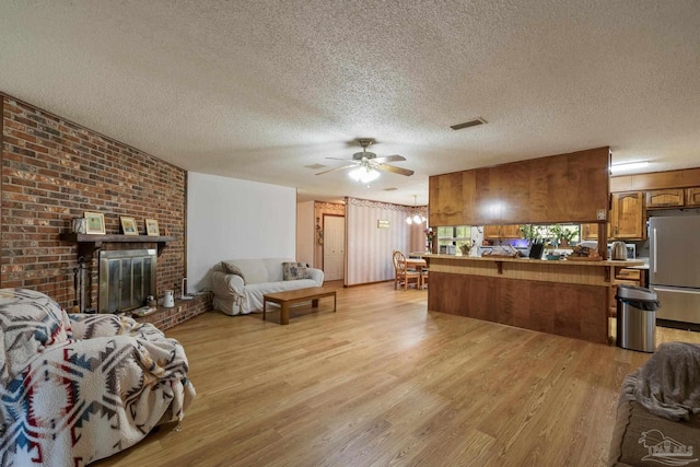 living area with a ceiling fan, a textured ceiling, visible vents, a brick fireplace, and light wood-style flooring