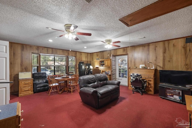 carpeted living room with attic access, a textured ceiling, ceiling fan, and wood walls