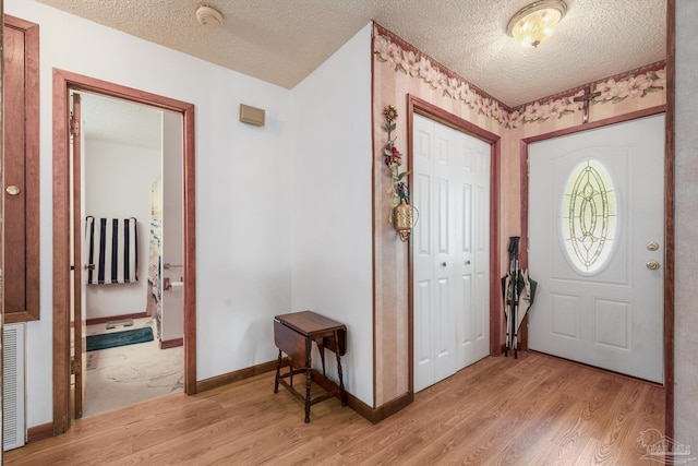foyer with light wood-type flooring, a textured ceiling, and baseboards