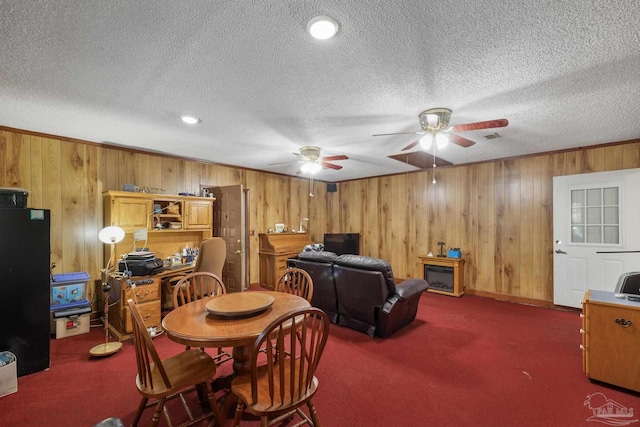 carpeted dining area featuring a ceiling fan, a textured ceiling, wood walls, and a fireplace