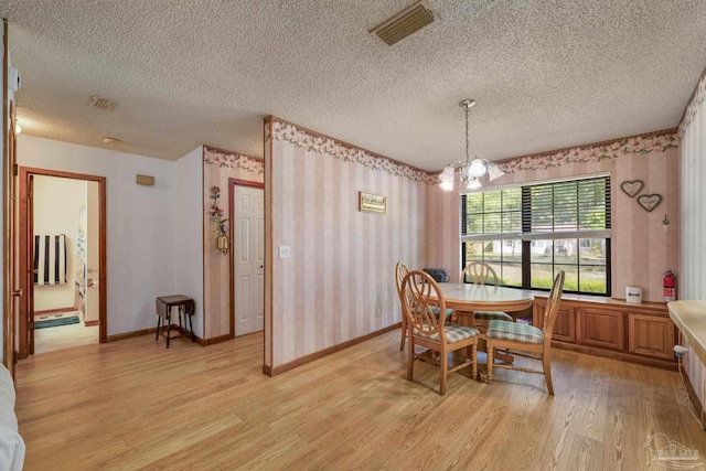 dining area with a textured ceiling, visible vents, wallpapered walls, and light wood finished floors