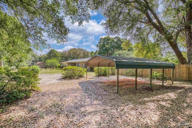 view of yard featuring fence, a carport, and dirt driveway