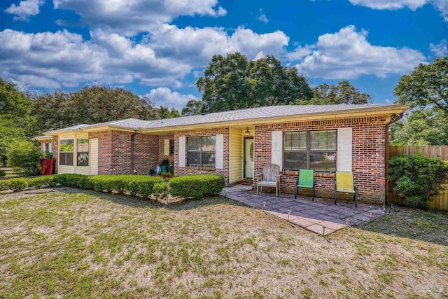 view of front of property featuring brick siding, fence, a patio, and a front lawn