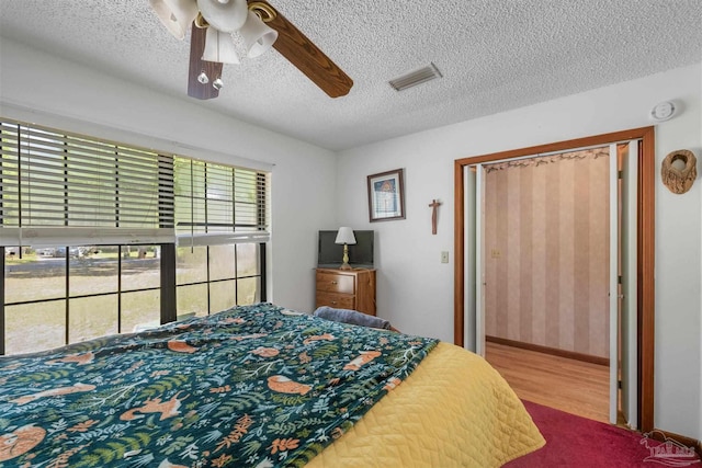 bedroom featuring ceiling fan, a textured ceiling, baseboards, wood finished floors, and visible vents