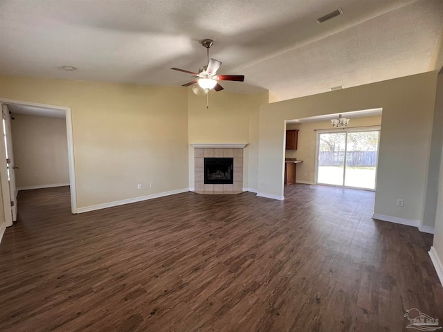 unfurnished living room featuring ceiling fan with notable chandelier, a textured ceiling, a tile fireplace, dark hardwood / wood-style flooring, and lofted ceiling