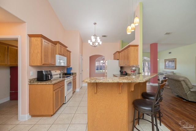 kitchen featuring arched walkways, a peninsula, white appliances, visible vents, and an inviting chandelier