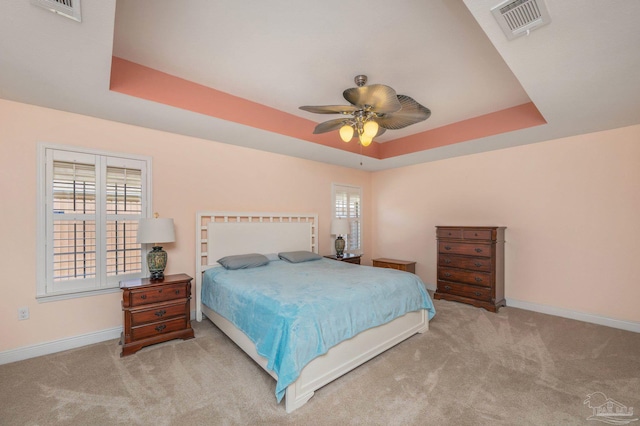 bedroom with a tray ceiling, visible vents, and carpet