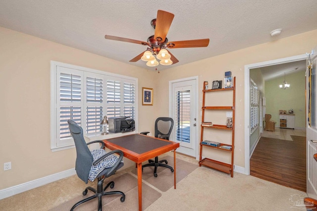 office area featuring a textured ceiling, ceiling fan with notable chandelier, baseboards, and light colored carpet