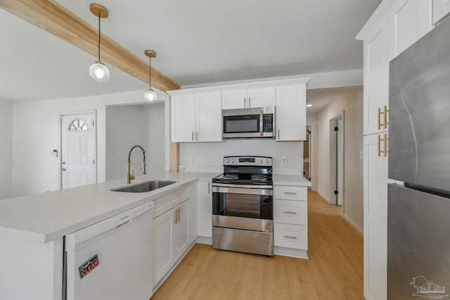 kitchen featuring white cabinets, appliances with stainless steel finishes, a sink, light countertops, and a peninsula