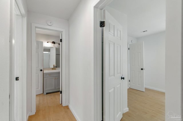 hallway featuring light wood-style floors, a sink, and baseboards