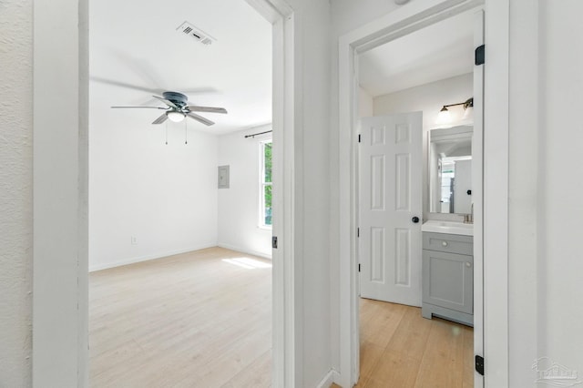 hallway featuring baseboards, a sink, visible vents, and light wood-style flooring