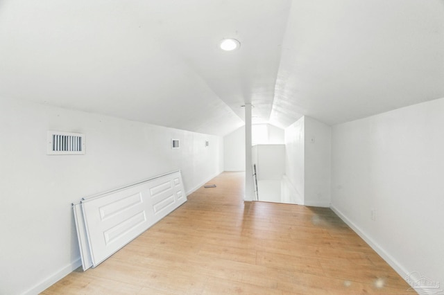 additional living space with light wood-style floors, baseboards, lofted ceiling, and visible vents