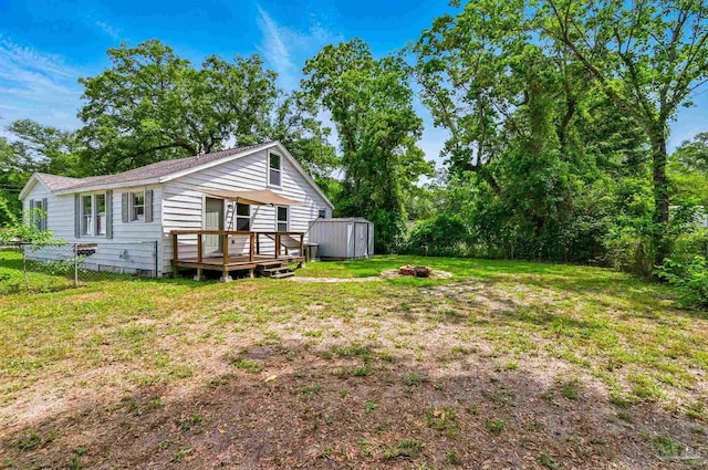 rear view of property featuring fence, a deck, a storage unit, an outbuilding, and a yard