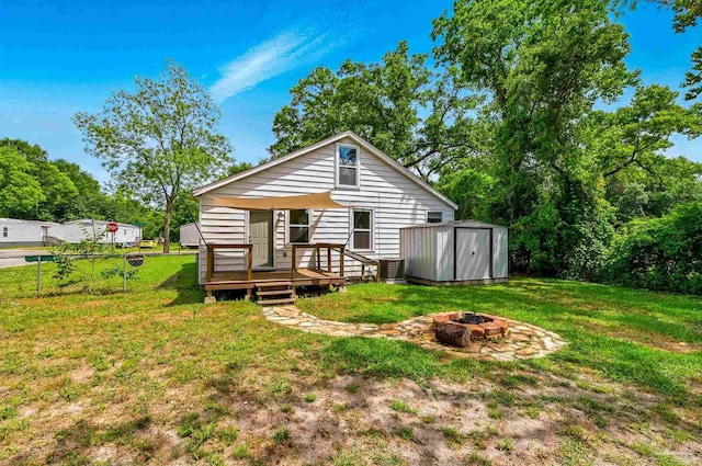 back of property featuring fence, a storage unit, a deck, a yard, and a fire pit