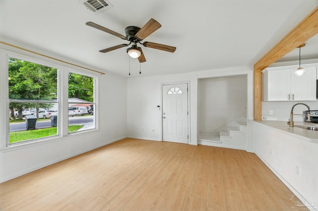 unfurnished living room with ceiling fan, visible vents, a sink, stairway, and light wood finished floors
