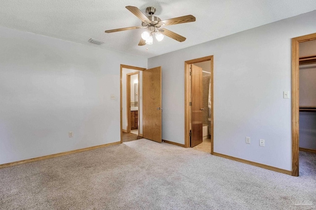 unfurnished bedroom featuring ceiling fan, connected bathroom, a walk in closet, light colored carpet, and a closet