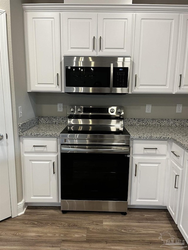 kitchen with light stone counters, appliances with stainless steel finishes, white cabinetry, and dark wood-type flooring