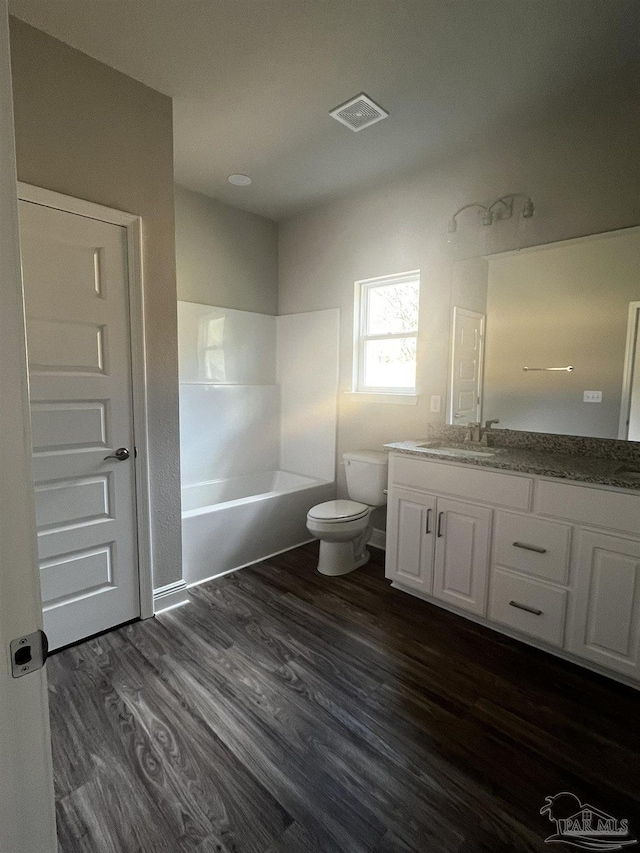 bathroom featuring visible vents, toilet, a bathing tub, wood finished floors, and vanity