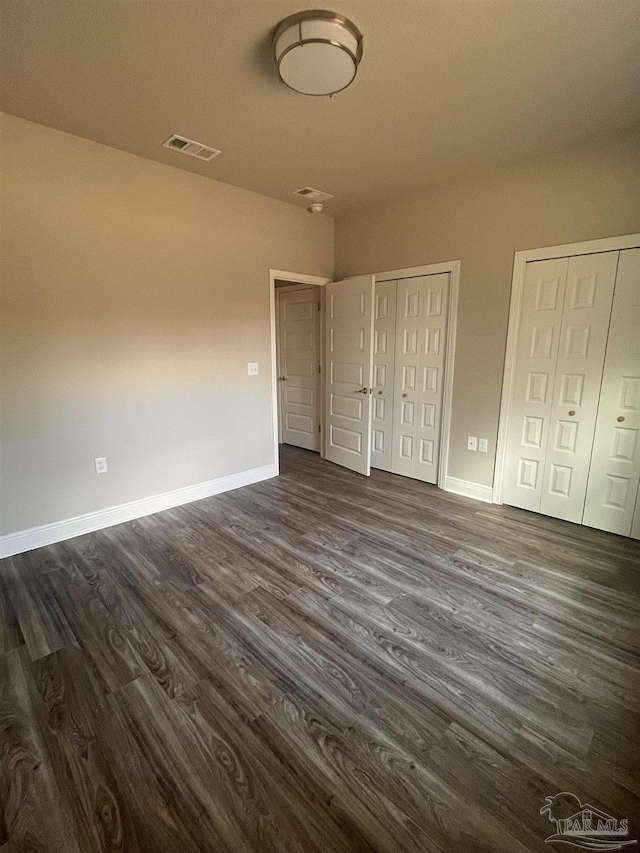 unfurnished bedroom featuring dark wood-style floors, visible vents, two closets, and baseboards