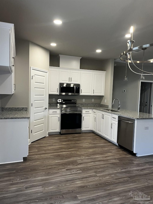 kitchen with a peninsula, dark wood-style flooring, a sink, appliances with stainless steel finishes, and white cabinetry