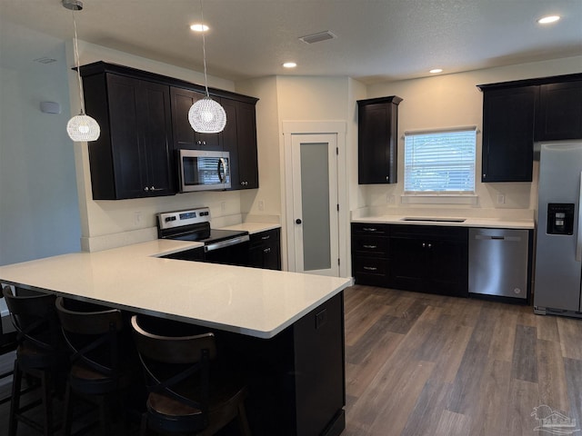 kitchen featuring dark wood-type flooring, a kitchen bar, hanging light fixtures, appliances with stainless steel finishes, and kitchen peninsula