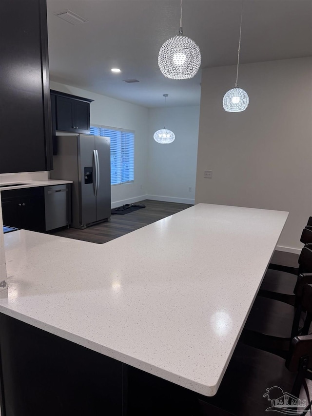 kitchen featuring a kitchen bar, decorative light fixtures, appliances with stainless steel finishes, dark hardwood / wood-style flooring, and kitchen peninsula