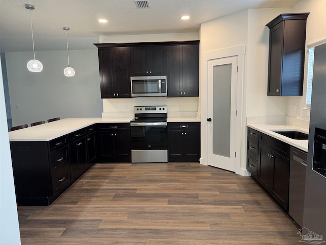 kitchen with sink, dark wood-type flooring, stainless steel appliances, decorative light fixtures, and kitchen peninsula