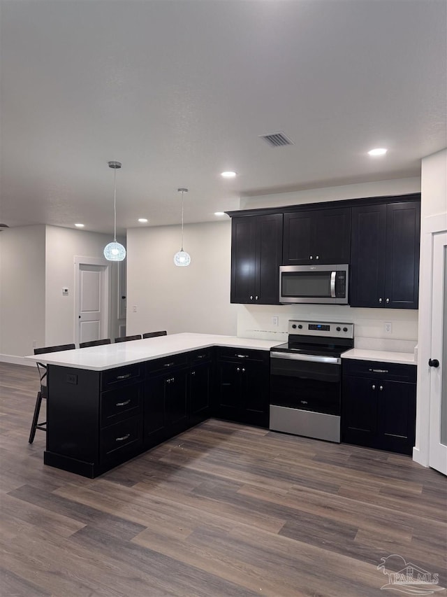 kitchen with appliances with stainless steel finishes, kitchen peninsula, dark hardwood / wood-style flooring, and decorative light fixtures