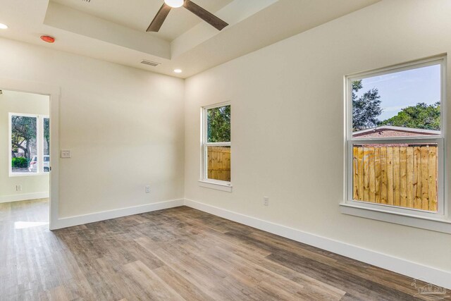 empty room featuring ceiling fan, wood-type flooring, and a tray ceiling