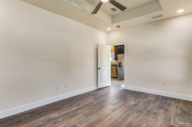 empty room featuring a raised ceiling, dark wood-type flooring, and ceiling fan