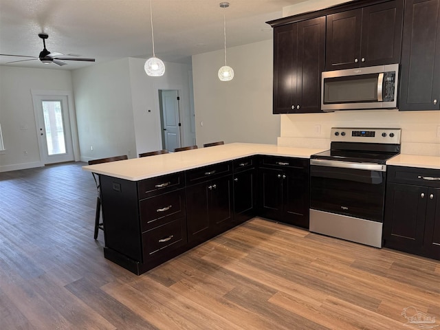 kitchen featuring pendant lighting, a breakfast bar area, appliances with stainless steel finishes, kitchen peninsula, and light wood-type flooring